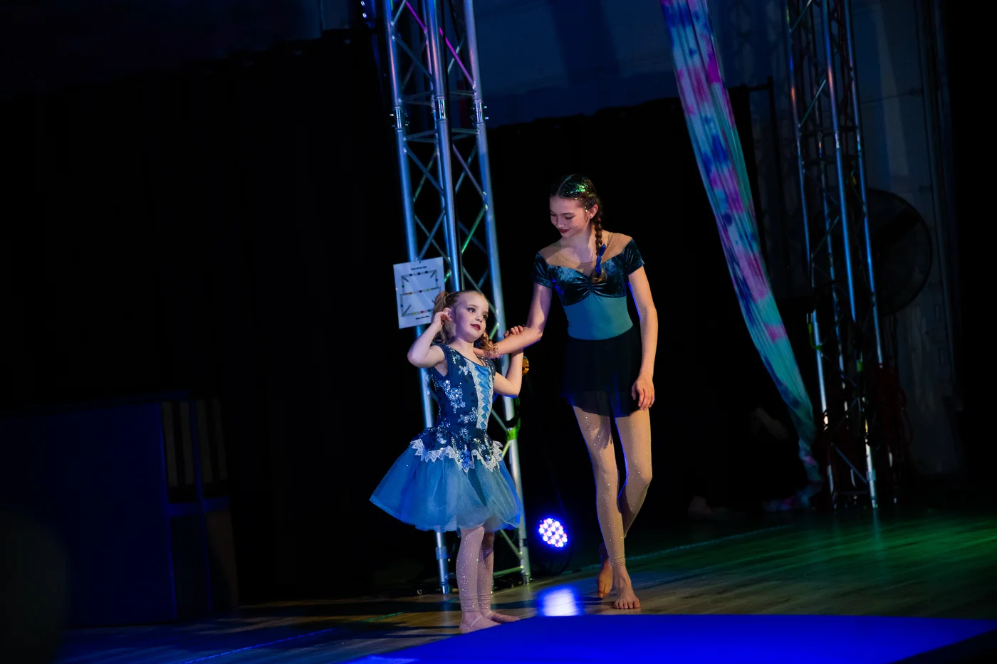 A young dancer and an older student in blue costumes together on stage during a Starbound showcase